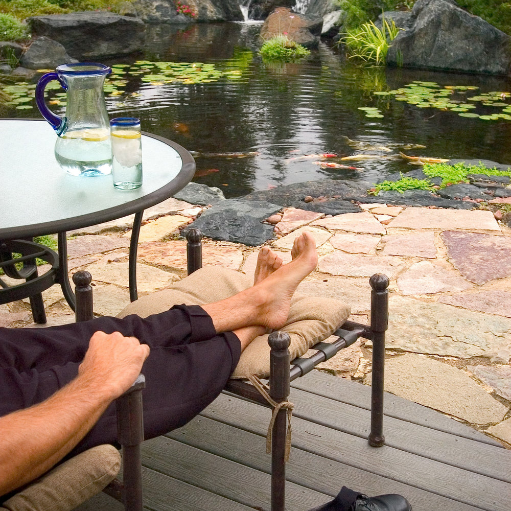 A man setting on hes patio next to a pond